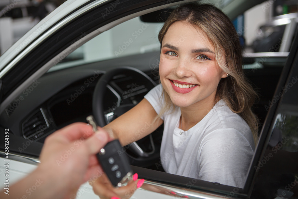 Beautiful happy woman sitting in her new automobile, receiving car keys from salesman