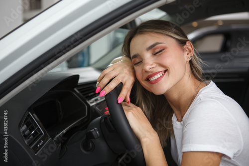 Beautiful happy woman smiling with her eyes closed, sitting in her new automobile, leaning on steering wheel © Ihor