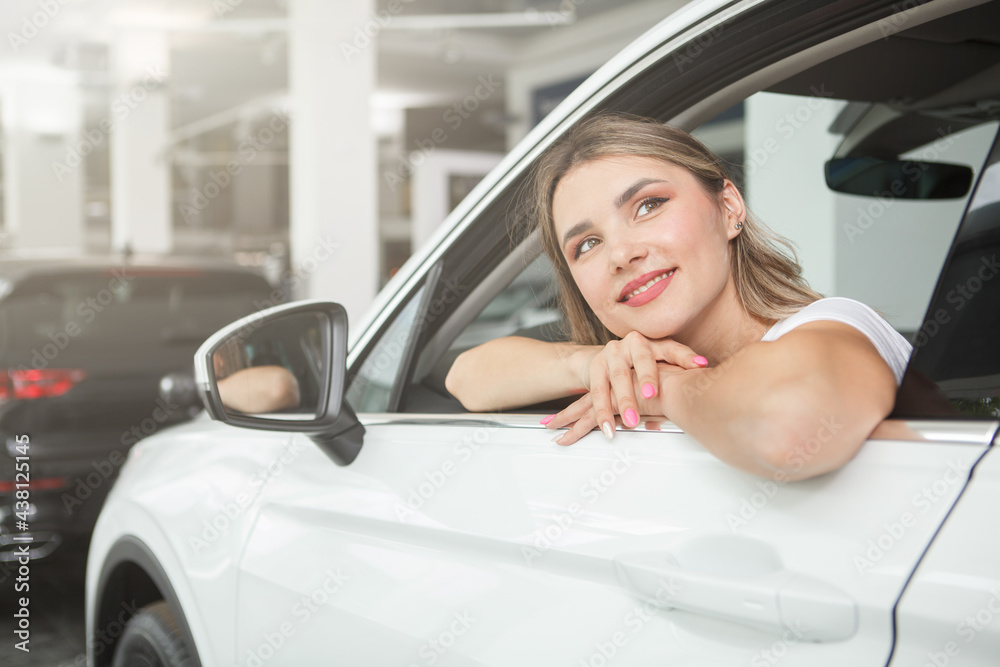 Charming young woman looking away dreamily, ditting in a new automobile at dealership