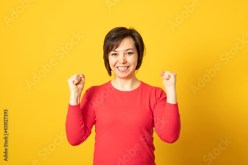 Life is wonderful! Joyful lady keeps fists clenched and exclaims in triumph, celebrates success, isolated over yellow background.