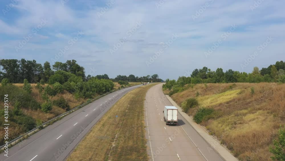 Aerial shot of truck with cargo trailer driving on motorway and transporting goods. Camera following to delivery lorry moving through country highway at sunny day. Flying over road traffic in rural Aerial shot of truck with cargo trailer driving on motorway and transporting goods. Camera following to delivery lorry moving through country highway at sunny day. Flying over road traffic in rural