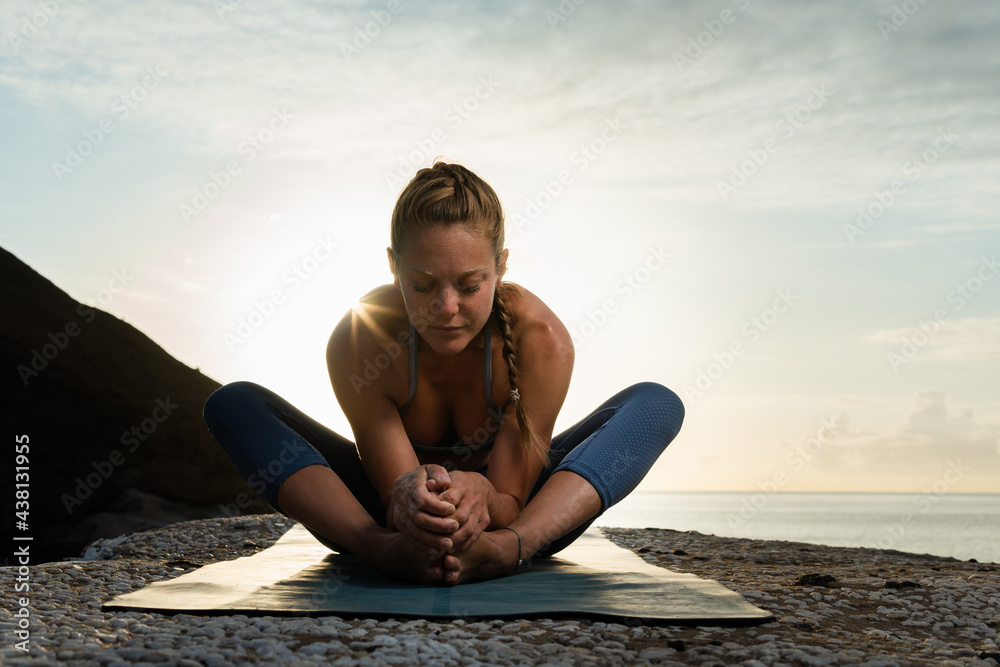 Woman performing forward bend on yoga mat against sea Woman performing forward bend on yoga mat against sea