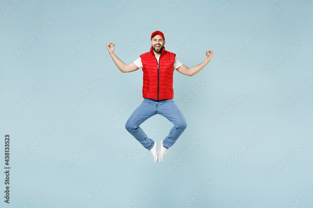 Obraz premium Full size body length side view delivery guy employee man in red cap white T-shirt vest uniform work dealer courier jump run go walk isolated on pastel blue color background studio. Service concept