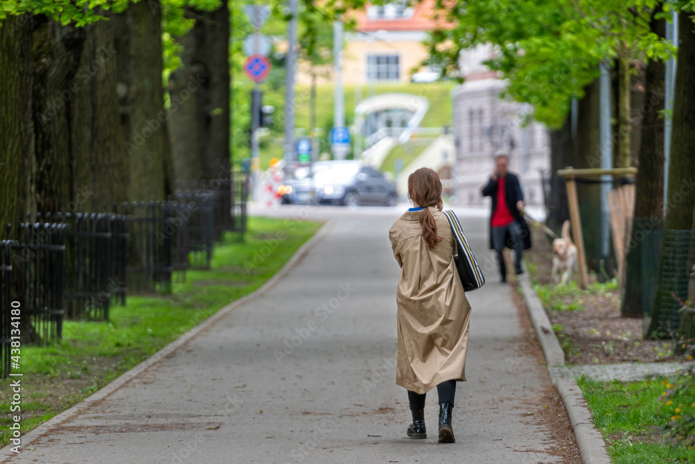 unrecognizable people walk down the sidewalk through a tree alley in a city park, back view unrecognizable people walk down the sidewalk through a tree alley in a city park, back view