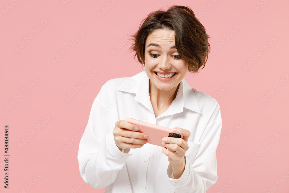 Young employee business woman corporate lawyer in classic formal white shirt work in office use play racing on mobile cell phone hold gadget smartphone video games isolated on pastel pink background Young employee business woman corporate lawyer in classic formal white shirt work in office use play racing on mobile cell phone hold gadget smartphone video games isolated on pastel pink background