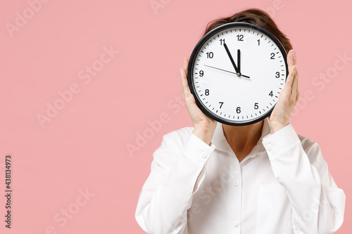 Young caucasian employee business secretary woman corporate lawyer in classic formal white shirt work in office hiding cover face with clock isolated on pastel pink color background studio portrait.