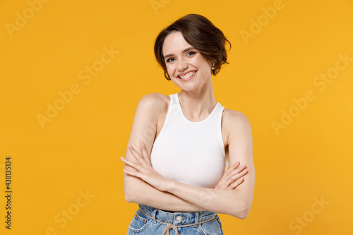 Foto Young smiling happy friendly caucasian woman 20s with bob haircut wearing white tank top shirt hold hands crossed folded isolated on yellow color background studio portrait