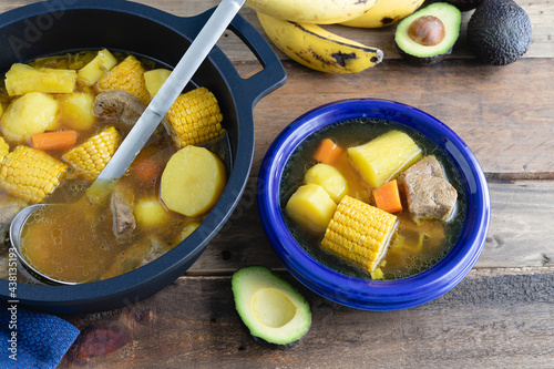 Blue plate with sancocho and pot on wooden background. Colombian cuisine concept. photo