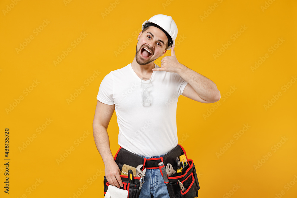 Young employee handyman man in protective helmet hardhat do phone gesture like say call me back isolated on yellow background Instruments accessories for renovation apartment room Repair home concept. Young employee handyman man in protective helmet hardhat do phone gesture like say call me back isolated on yellow background Instruments accessories for renovation apartment room Repair home concept.