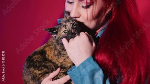 A young woman of informal appearance hugs a tortoiseshell cat. The rocker girl loves to pet her pet.