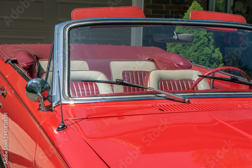 Close up partial view of a vintage 1960s red convertible with the top down.  Looking through the windshield to the red and white leather seats.