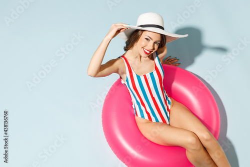 Top view young sexy woman slim body wear striped one-piece swimsuit widebrim hat lies inflatable tube ring hotel pool isolated on pastel blue color background Summer vacation sea rest sun tan concept photo