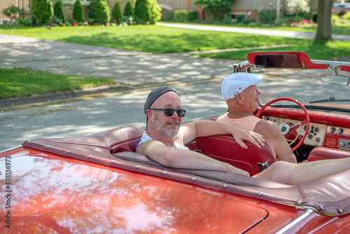 Father and son out for a Sunday drive in an old 1960s red convertible, with dad driving and son relaxing  in the back seat and his feet stretched out of the car.