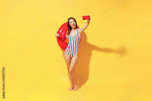 Full length happy young sexy woman slim body wear red blue swimsuit posing with inflatable rubber ring isolated on vivid yellow color wall background studio Summer hotel pool sea rest sun tan concept
