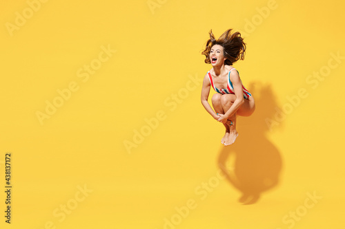 Full length happy young sexy woman slim body wear striped red blue one-piece swimsuit jump dive into water isolated on vivid yellow color background studio. Summer hotel pool sea rest sun tan concept.