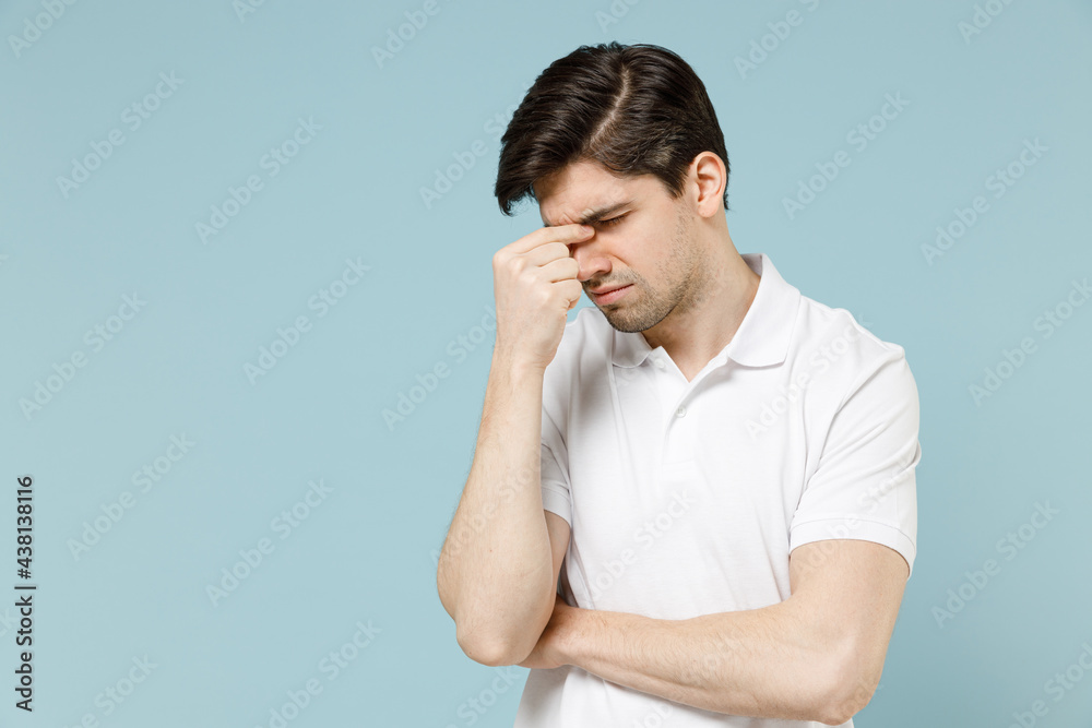 Young confused puzzled pensive sick unshaven caucasian man 20s in white casual basic t-shirt keep eyes closed rub put hand on nose isolated on pastel blue background studio. People lifestyle concept. Young confused puzzled pensive sick unshaven caucasian man 20s in white casual basic t-shirt keep eyes closed rub put hand on nose isolated on pastel blue background studio. People lifestyle concept.