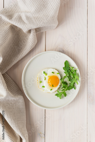 Fried eggs with green onions and arugula on a plate on a wooden table. Vertical orientation, top view.
