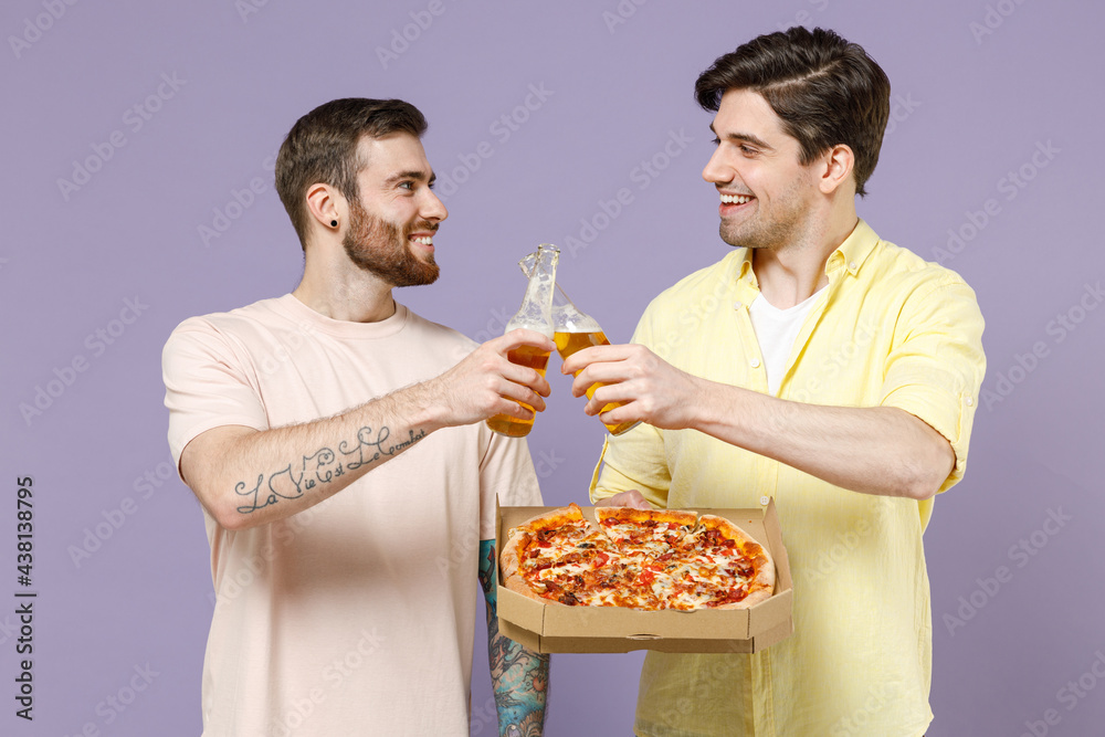 Two happy cool young men friends together in casual t-shirt tattoo translate fun eat italian pizza in cardboard flatbox drink beer clink isolated on purple background studio People lifestyle concept Two happy cool young men friends together in casual t-shirt tattoo translate fun eat italian pizza in cardboard flatbox drink beer clink isolated on purple background studio People lifestyle concept