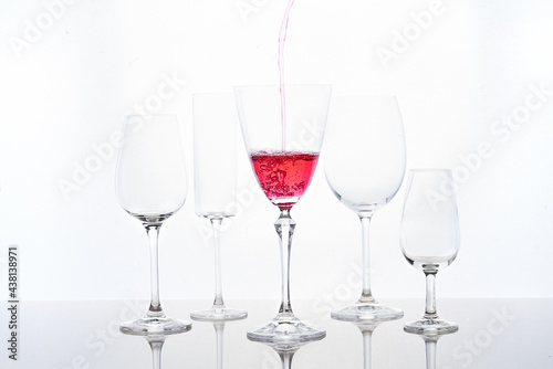 Red cocktail filling into goblet placed near different crystal glasses photo