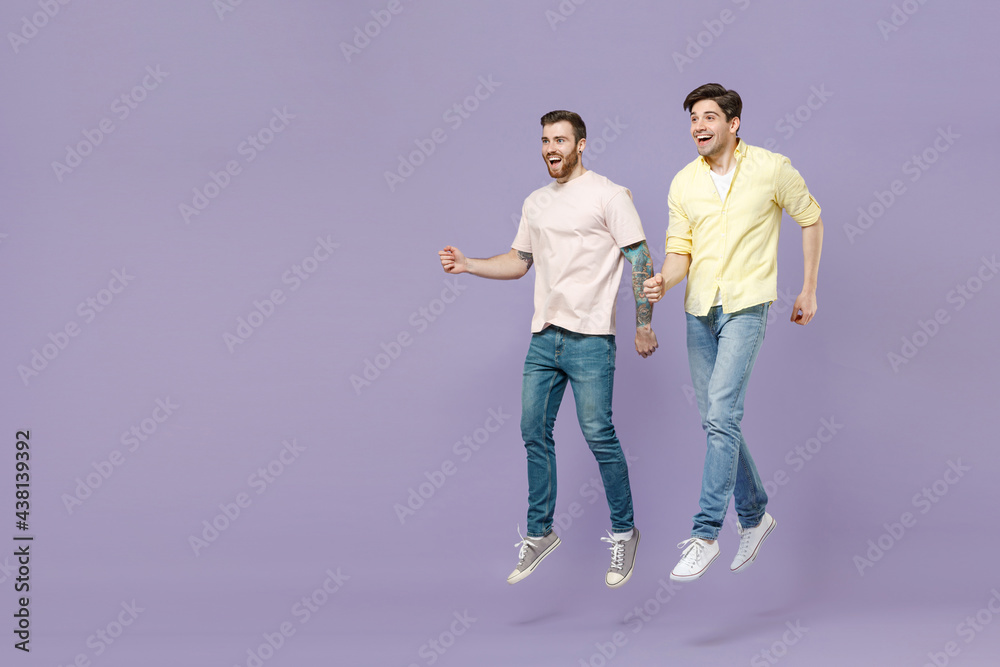 Full length overjoyed excited amazed two young happy men friends together walking in casual t-shirt jumping high look aside isolated on purple background studio People friendship lifestyle concept