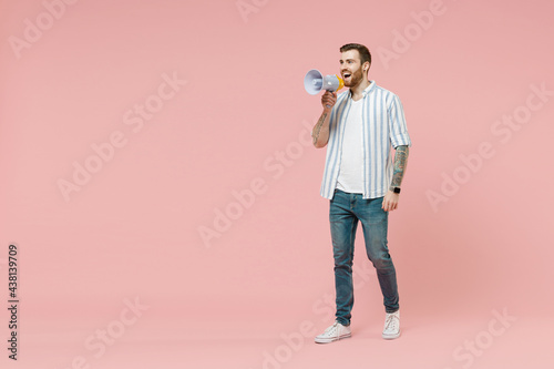 Full body young caucasian unshaven man 20s wear blue striped shirt whote t-shirt screaming loud shouting in megaphone isolated on pastel pink color background studio portrait. Tattoo translate fun