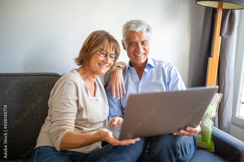 happy older couple sitting on sofa with laptop computer