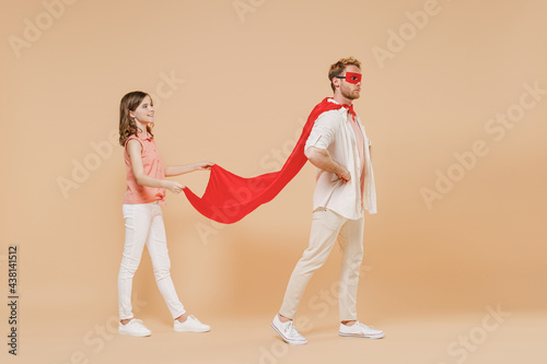 Full length side view powerful father man in superhero suit, have supernatural abilities, enjoy free time together with kid teen daughter walk isolated on beige background. Real heroes defend you