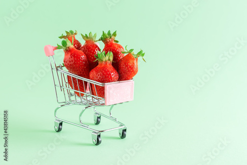 Fresh strawberries in a small shopping cart. Pastel green background. Creative layout. Selective focus.
