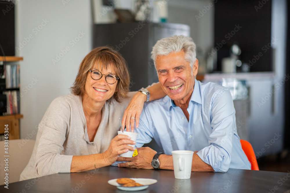 smiling mature couple sitting at table with cup of tea smiling mature couple sitting at table with cup of tea