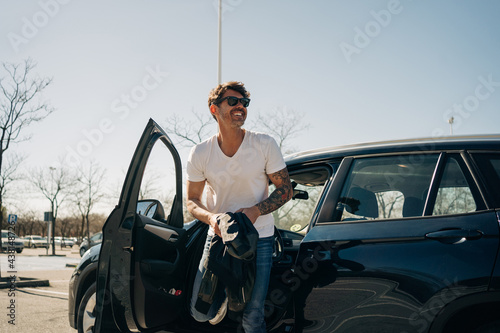 Smiling tattooed man getting out of automobile in sunlight photo