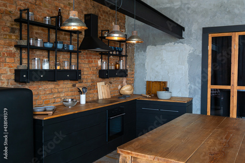 View on a wooden table and open space industrial loft kitchen with vintage decor and black cabinets