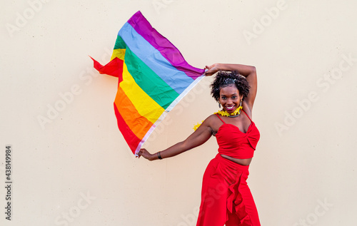 Stylish black woman with LGBTQ flag on light background photo