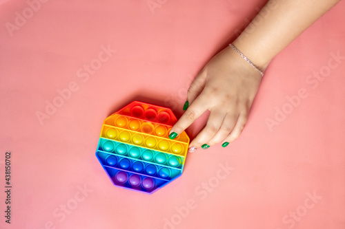 female hand playing with rainbow toy antistress pop it