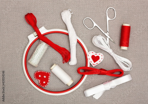 The embroidery hoop, red and white sewing threads, ribbons, beads on canvas background