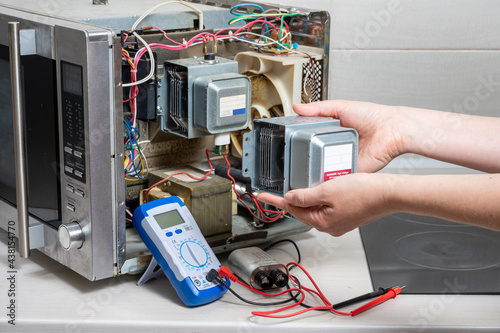 Repair of the microwave oven. The woman shows the new magnetron. photo