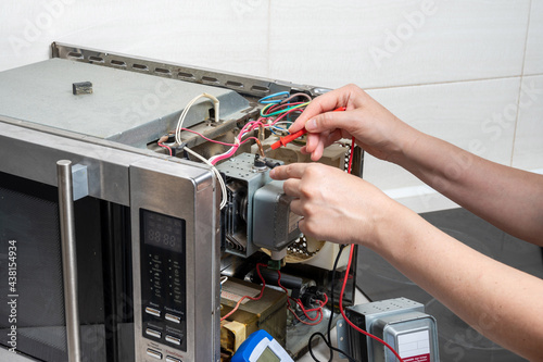Repair of the microwave oven. A woman measures the electrical characteristics with a tester.