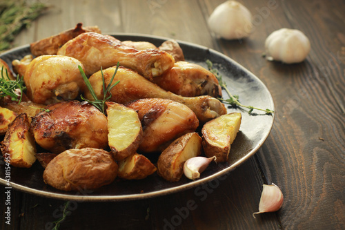 Fried chicken legs with spices and fried potatoes in a plate on the wooden table close up.