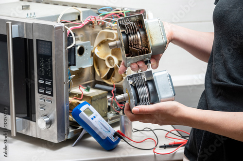 Repair of the microwave oven. The woman shows the old and new magnetrons. photo
