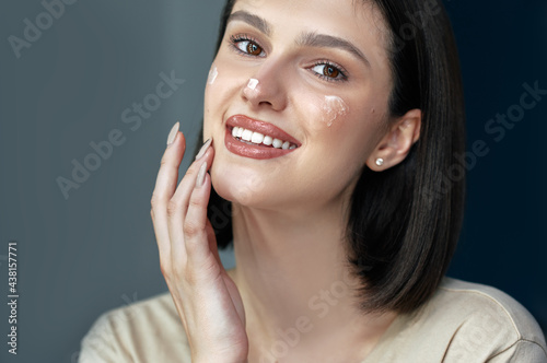 Closeup portrait of a gorgeous female applying cream on her face. Brunette young woman using moisturizing cream.