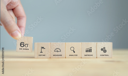 Hand pick up Six sigma icon on wooden cubes standing on wood table with blue background, clean tone. The DMAIC Industrial technology quality control, industrial process improving and lean concept.