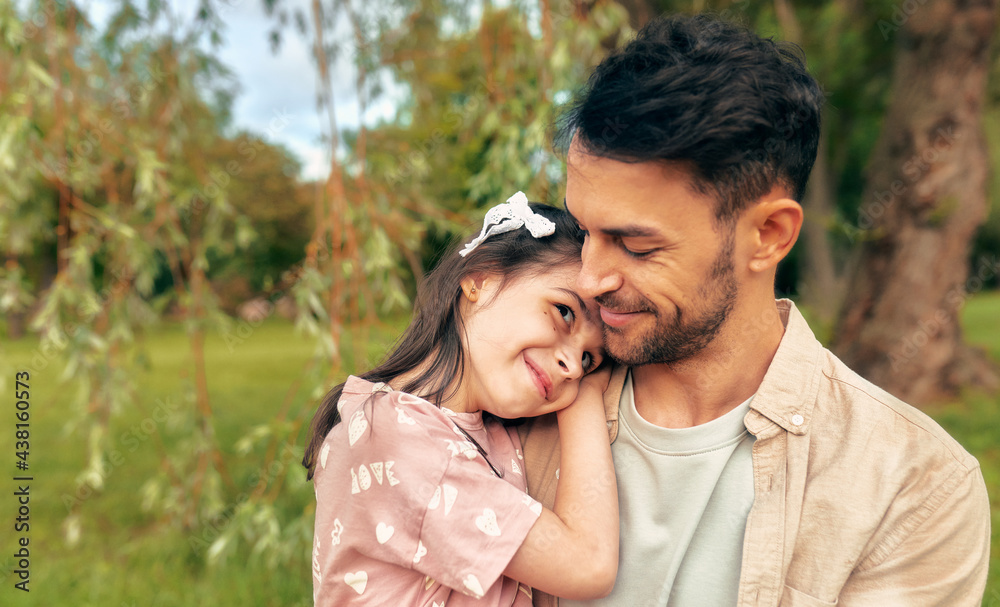 Fototapeta premium Portrait of a smiling father embracing his little daughter in the park.