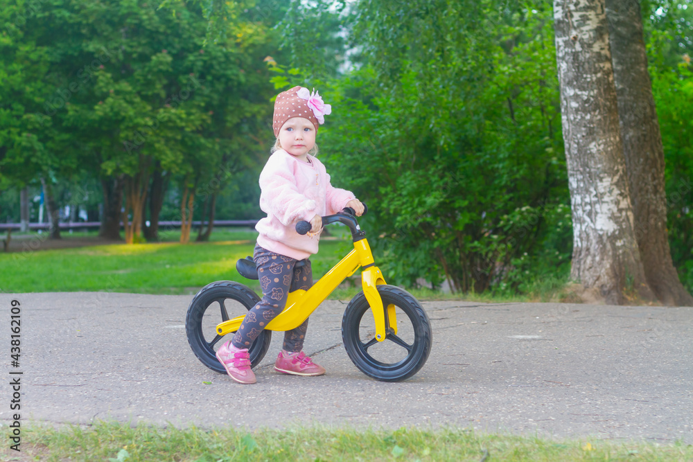 A child girl rides in the park on a yellow running bike in summer or spring
