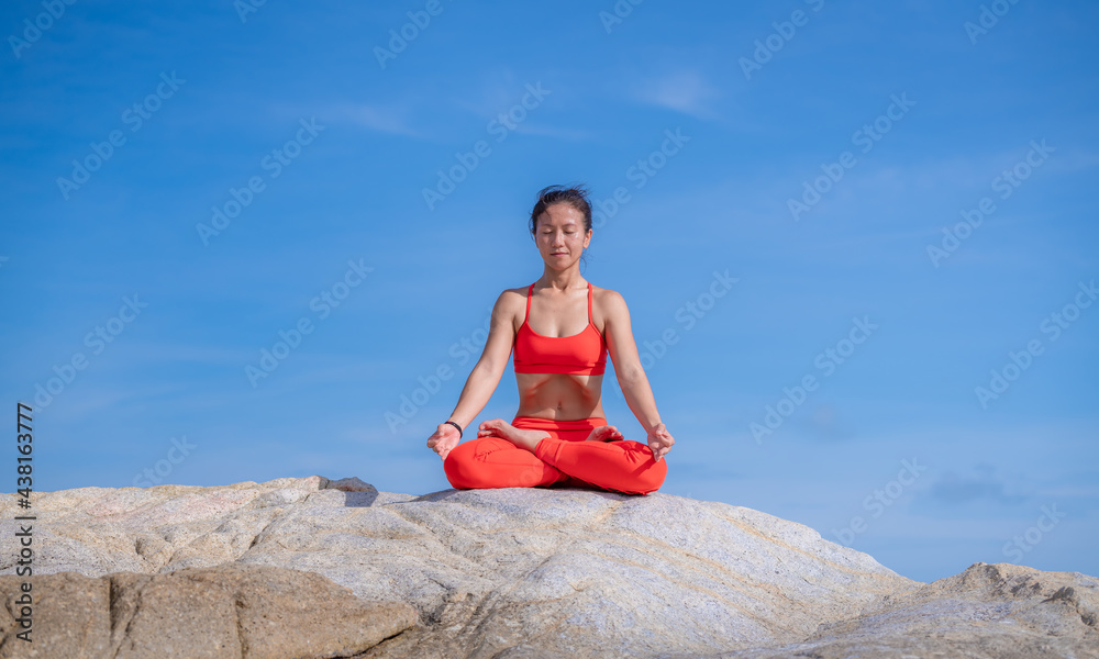 Asian young healthy woman posing practice yoga on stone  beach with blue cloud sky and sea background in healthy exercise lifestyle concept.