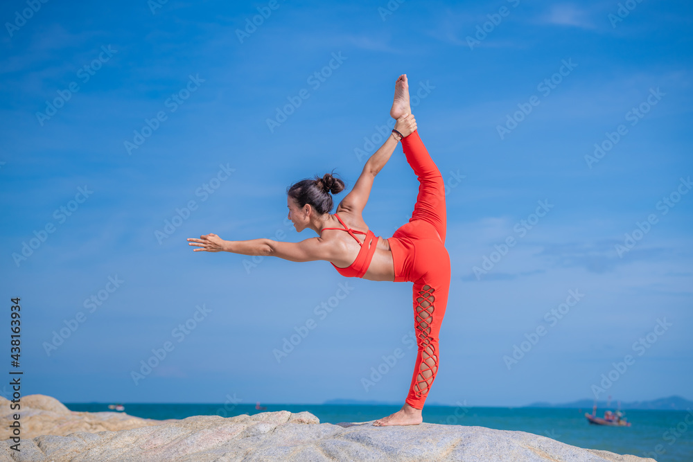 Asian young healthy woman posing practice yoga on stone  beach with blue cloud sky and sea background in healthy exercise lifestyle concept.