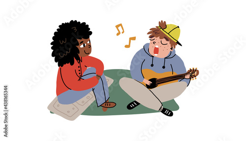 A cute guy serenades his girlfriend and plays the guitar. Couple or friends spending time outdoors. 