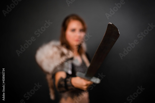 Medieval woman warrior in chain mail armor and polar fox fur on her shoulders standing with a sword in hand on a dark background. Fantasy barbarian, viking.