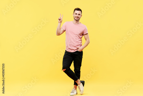 Full length portrait of trendy handsome man show victory sign on yellow background