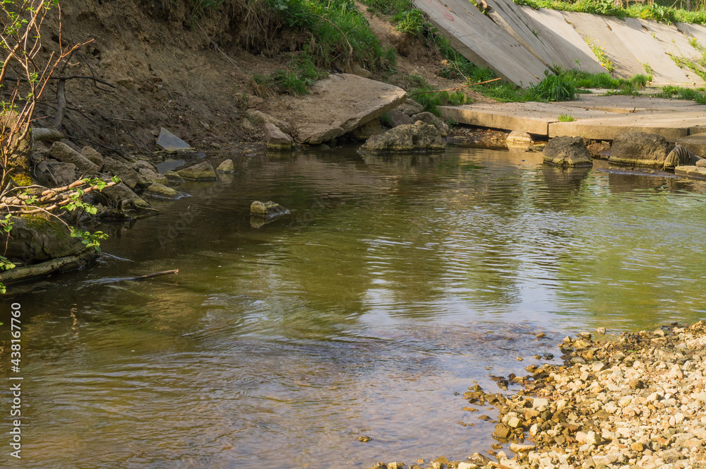 Close-up photo of a small river (stream) polluted with broken concrete slabs.