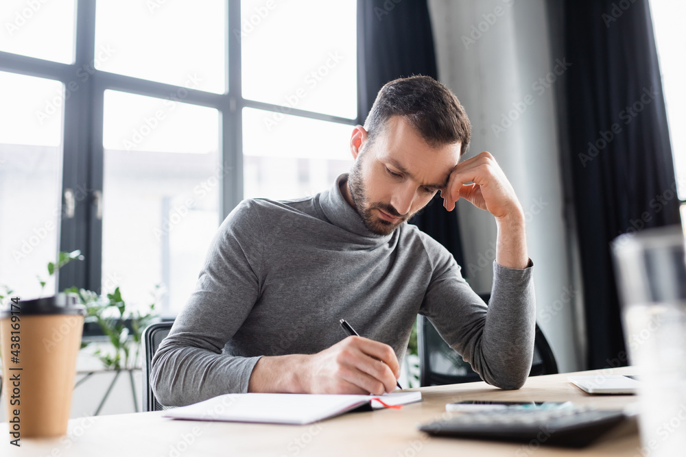 Businessman writing on notebook near smartphone and blurred coffee to go Businessman writing on notebook near smartphone and blurred coffee to go