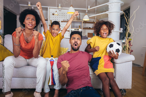 Happy african american family watching soccer match on television in living room at home. © Mediteraneo